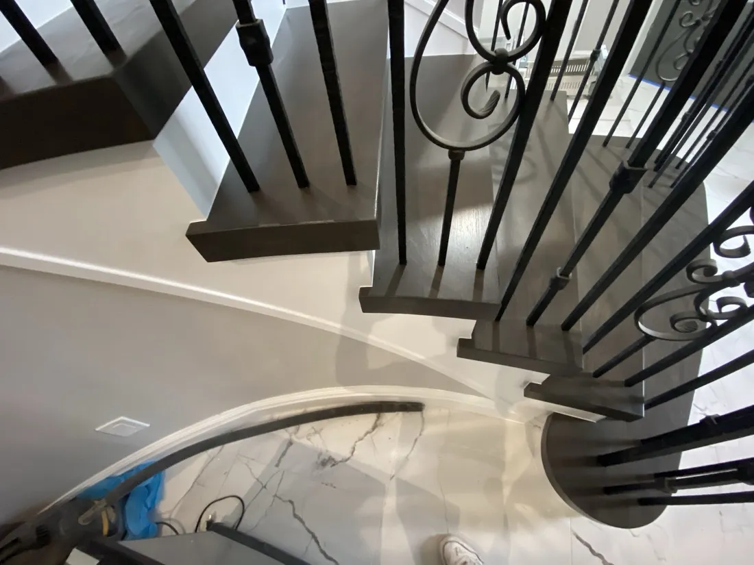 Curved staircase with dark treads and wrought iron balusters