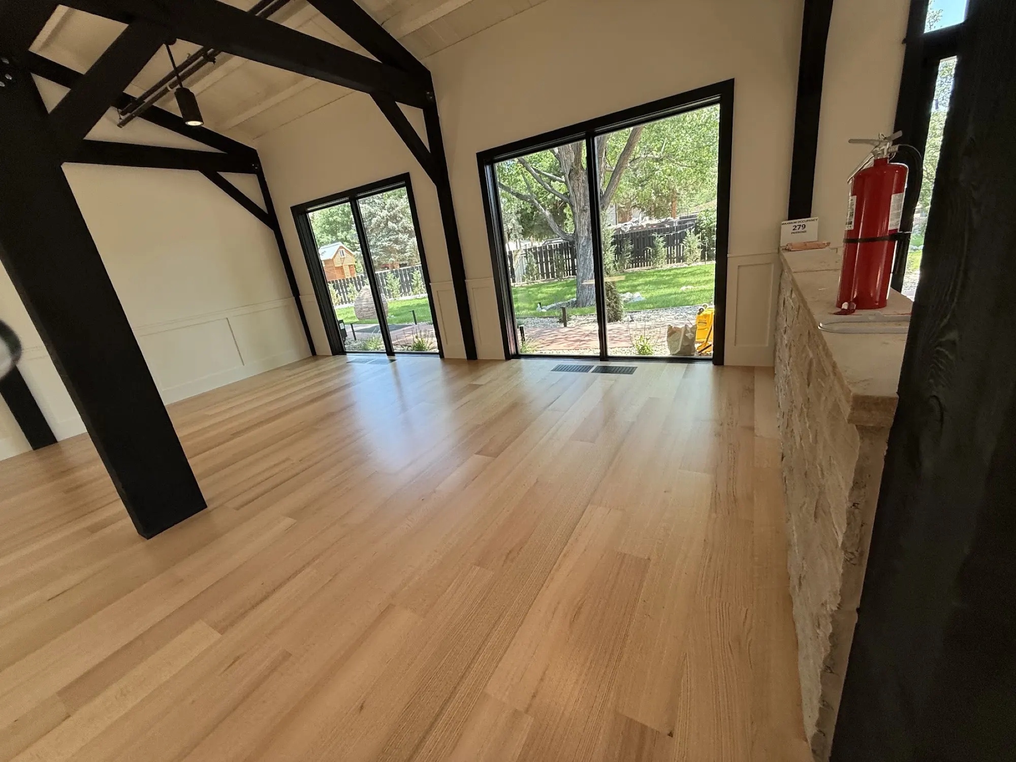 Refinished white oak floor running through an open great room with exposed timber beams
