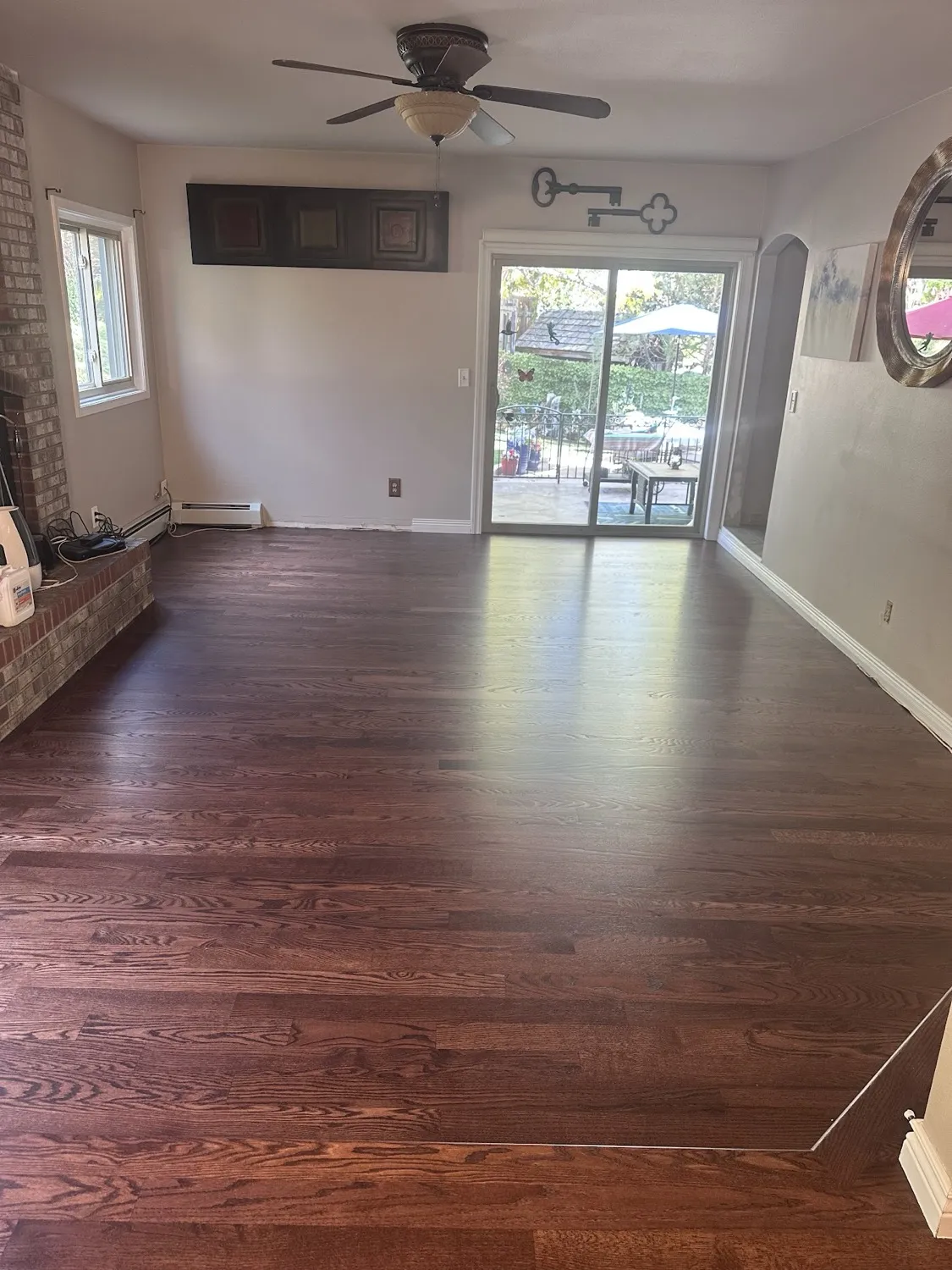 Living room floor refinished in a deep red-brown stain beside a brick fireplace